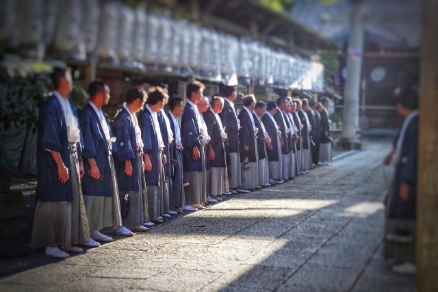 神事の朝、揃いの着物を着た20人以上の男性が、神社の参道脇に整列して、一斉に本殿の方を見ている